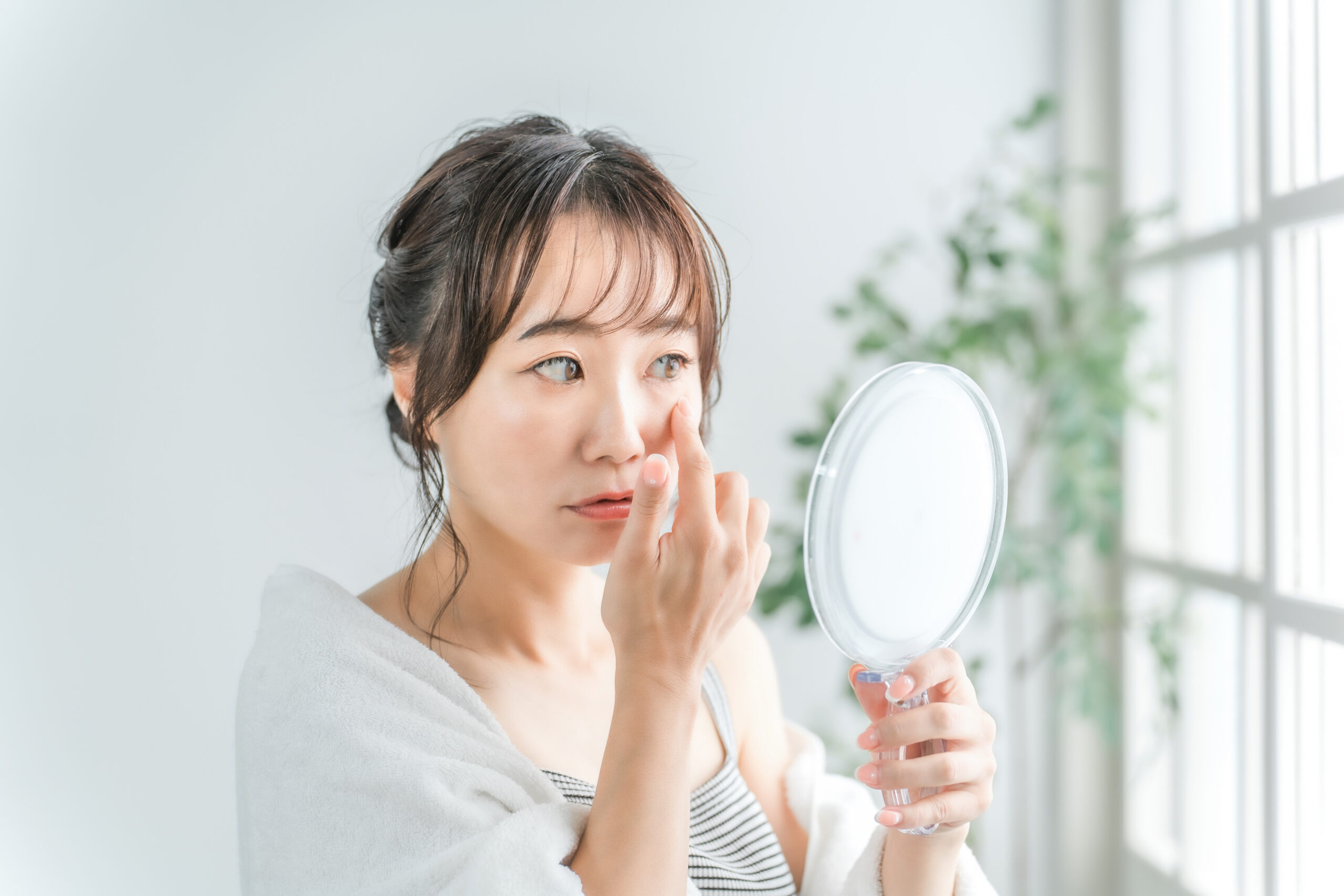 鏡で自分の目元の状態を確認する女性の写真