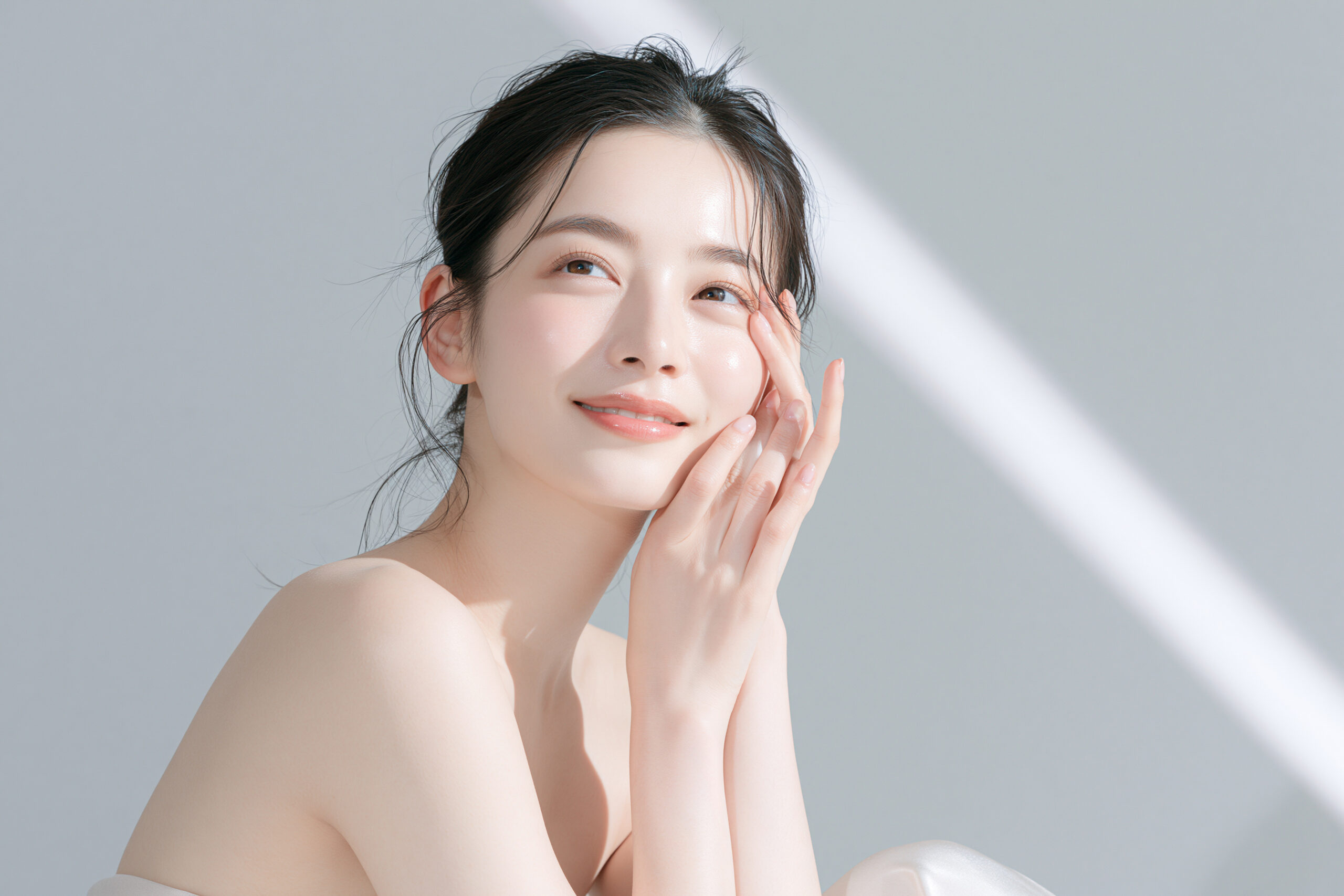 ラコスによる透明感のある肌をイメージした、頬に両手を添えて微笑む女性の写真